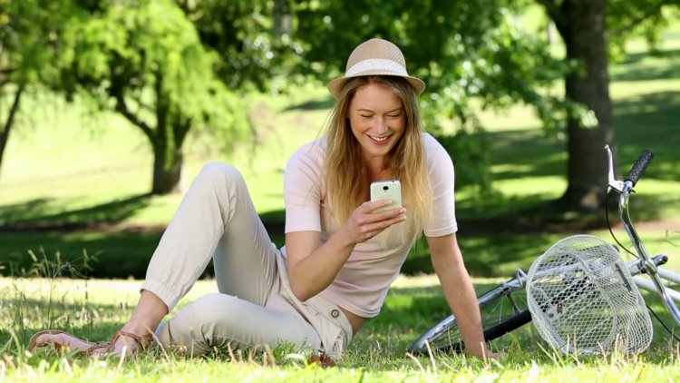 stock-footage-pretty-girl-using-smartphone-beside-her-bike-in-the-park-on-a-sunny-day