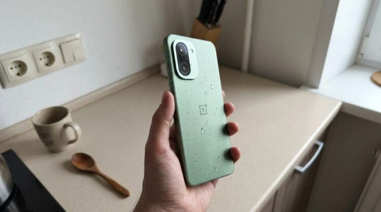 Смартфон OnePlus в руке, капли воды на корпусе